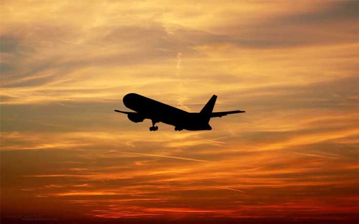 silhouette plane taking off against an orange sky